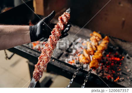 Chef preparing minced meat kebab skewer for grilling over open flame, a classic barbecue delicacy Chef preparing minced meat kebab skewer for grilling over open flame, a classic barbecue delicacy 120087357