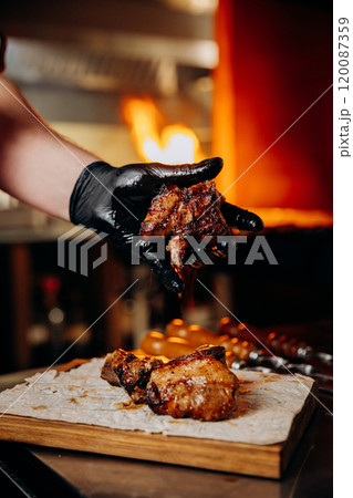 Chef holding grilled meat piece over flatbread, capturing the essence of flame-grilled flavor 120087359