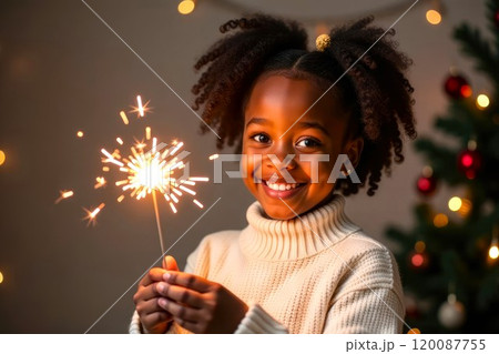 Happy Curly Girl Holding burning Sparkler by a lit Christmas tree. Child smiling and holding burning Sparkler blast, holiday celebration event party 120087755