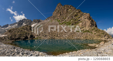 Clear mountain lake reflecting rugged cliffs and snow capped peaks in alpine landscape Clear mountain lake reflecting rugged cliffs and snow capped peaks in alpine landscape 120088603