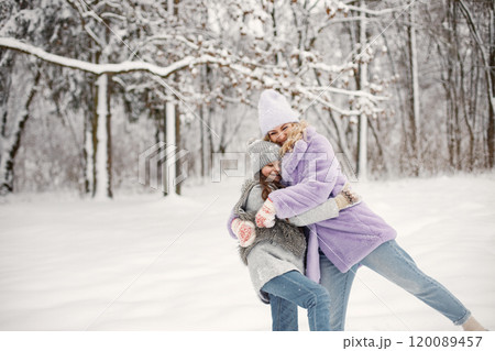 Young blonde woman with her daughter playing in winter in a snowballs. Caucasian woman wearing purple warm jacket and knitted hat. Brunette girl wearing grey jacket and hat. Young blonde woman with her daughter playing in winter in a snowballs. Caucasian woman wearing purple warm jacket and knitted hat. Brunette girl wearing grey jacket and hat. 120089457