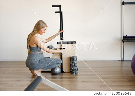Pregnant woman doing exercises with a special equipment. Fit blonde woman working out in a gym. Woman wearing black sportive leggins and top. Pregnant woman doing exercises with a special equipment. Fit blonde woman working out in a gym. Woman wearing black sportive leggins and top. 120089543