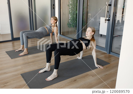 Two pegnant women doing stretching exercise. Fit blonde and brunette women working out in a gym. Women wearing grey and black sportive leggins and tops. 120089570