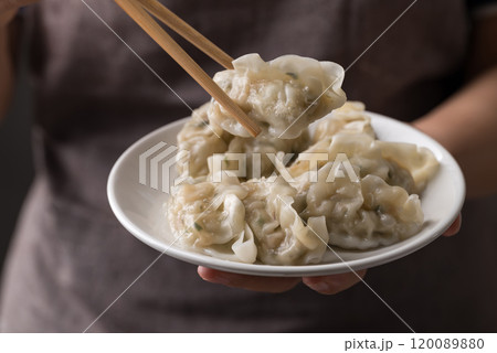 Hand holding chopsticks and eating steamed dumpling filled with pork and vegetables on dish 120089880
