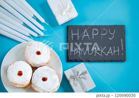 Happy Hanukkah. Jewish dessert sufganiyot donuts on blue background. Symbol of religious Judaism holiday. Inscription on chalk board. Happy Hanukkah. Jewish dessert sufganiyot donuts on blue background. Symbol of religious Judaism holiday. Inscription on chalk board. 120090030