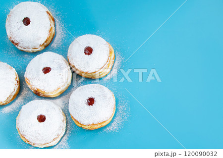 Symbols of Jewish religious holiday Hanukkah. Traditional dessert donuts sufganiyot on blue background. Symbols of Jewish religious holiday Hanukkah. Traditional dessert donuts sufganiyot on blue background. 120090032