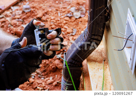 Electric wires being held by an electrician while fixing an outlet plug on outside of wall Electric wires being held by an electrician while fixing an outlet plug on outside of wall 120091267
