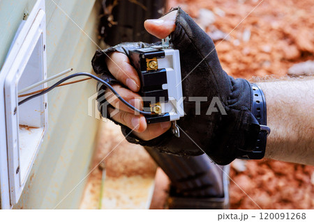 Hand of electrician holding electric wires for outlet plug fixing in outside wall Hand of electrician holding electric wires for outlet plug fixing in outside wall 120091268