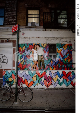 A couple poses by a colorful heart mural in the city, happily enjoying each other 120092184