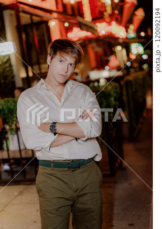 A Stylish Young Man is Posing Outdoors Under the Night Sky in a Vibrant City Setting A Stylish Young Man is Posing Outdoors Under the Night Sky in a Vibrant City Setting 120092194