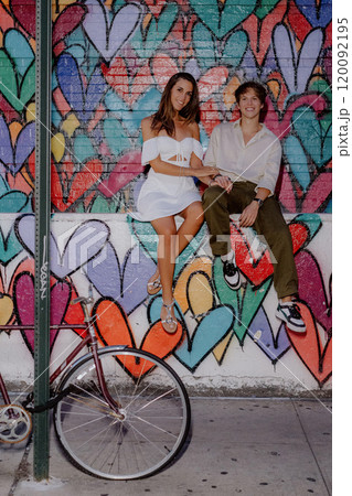 A couple poses by a colorful heart mural in the city, happily enjoying each other 120092195