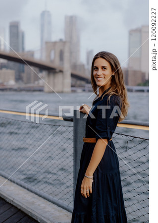 A Stylish Woman Posing by the Water with a Beautiful Cityscape in the Background A Stylish Woman Posing by the Water with a Beautiful Cityscape in the Background 120092227