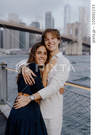 A couple embraces at the iconic Brooklyn Bridge, enjoying the breathtaking city skyline 120092233
