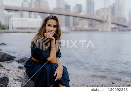 A woman stands gracefully by the sparkling water with a stunning city skyline in the background 120092238
