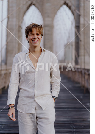 A Young Man is Joyfully Smiling on the Iconic Brooklyn Bridge While Dressed Casually 120092262