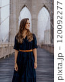 A woman in a stylish dress strikes a captivating pose on the iconic Brooklyn Bridge 120092277