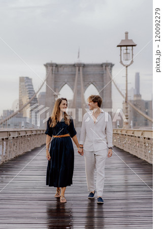 A couple is walking hand in hand across the Brooklyn Bridge as the sun rises beautifully A couple is walking hand in hand across the Brooklyn Bridge as the sun rises beautifully 120092279