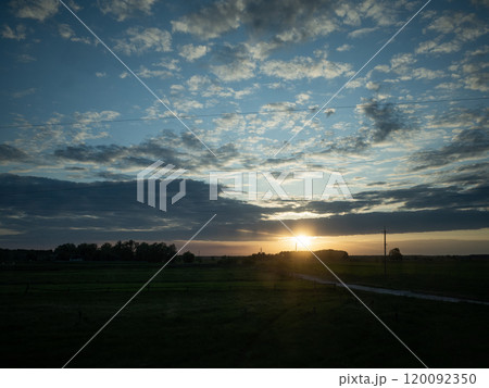 【ウクライナ】郊外の地平線に沈みゆく太陽と青空に漂う雲 120092350