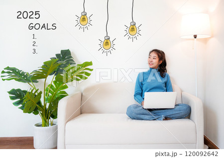 2025 goals with young woman pointing goals cheerful and happy new year with laptop on the sofa in living room 2025 goals with young woman pointing goals cheerful and happy new year with laptop on the sofa in living room 120092642