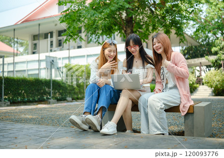 Three women sitting on a bench, one of them looking at a laptop Three women sitting on a bench, one of them looking at a laptop 120093776