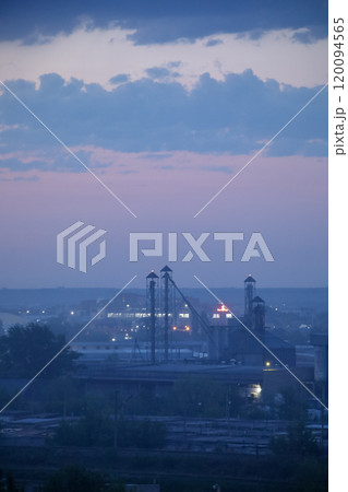 Twilight Industrial Landscape featuring Smokestacks and a Vibrant City Skyline at Dusk Twilight Industrial Landscape featuring Smokestacks and a Vibrant City Skyline at Dusk 120094565