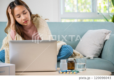 Unwell female working online feeling sick unhealthy, Sick young business woman on sofa suffering from coronavirus covered blanket still work with laptop at home, influenza symptoms, medicine on desk Unwell female working online feeling sick unhealthy, Sick young business woman on sofa suffering from coronavirus covered blanket still work with laptop at home, influenza symptoms, medicine on desk 120096043