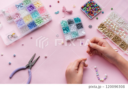 Creating colorful beaded jewelry with assorted beads and crafting tools on a light pink surface Creating colorful beaded jewelry with assorted beads and crafting tools on a light pink surface 120096308