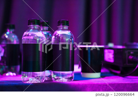 Plastic water bottles with blank black labels in the dark and purple lighting. Plastic water bottles with blank black labels in the dark and purple lighting. 120096664