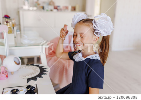 A little girl in a school uniform preens herself at a dressing table.  120096808