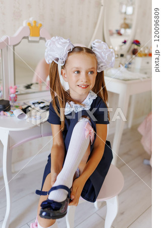 A little girl in a school uniform puts on shoes at a dressing table.  120096809