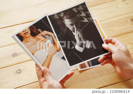 Men's hands put on the wooden table and show wedding photos. 120096814