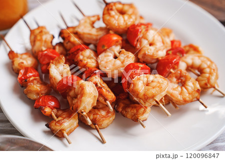 Skewers with shrimps and tomatoes on a white plate.  120096847