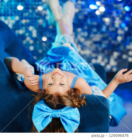 Cute teenage girl in blue doll dress with big blue bow posing in an armchair Cute teenage girl in blue doll dress with big blue bow posing in an armchair 120096876