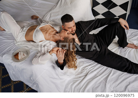 A man and a woman in silk pajamas are lying on a bed. 120096975