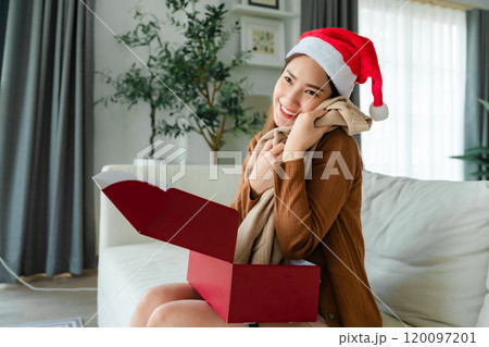 Young Asian woman wearing Christmas hat and opening a gift box 120097201