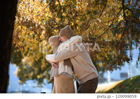 Portrait of beautiful senior couple during walk in autumn park. Elderly husband and wife are embracing each other. 120099059