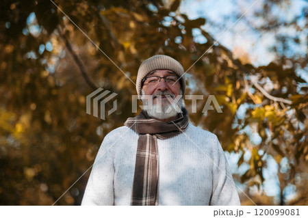 Portrait of smiling older man with a gray beard. Senior standing outdoors in nature, looking at camera. 120099081
