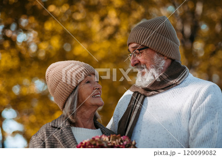 Portrait of beautiful senior couple during walk in autumn park. Elderly husband and wife are looking at each other lovingly. 120099082