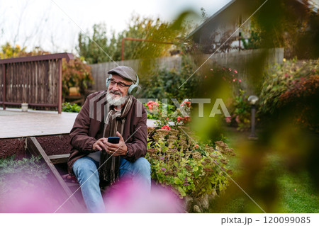 Older man with a gray beard having moment for himself, listening music. Senior wearing headphones and playing music from phone. Older man with a gray beard having moment for himself, listening music. Senior wearing headphones and playing music from phone. 120099085