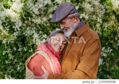 Portrait of beautiful senior couple outdoors in an autumn garden. Elderly husband and wife are embracing each other. 120099096