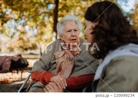Disabled elderly woman in wheelchair holding hands with her caregiver, talking. Disabled elderly woman in wheelchair holding hands with her caregiver, talking. 120099234