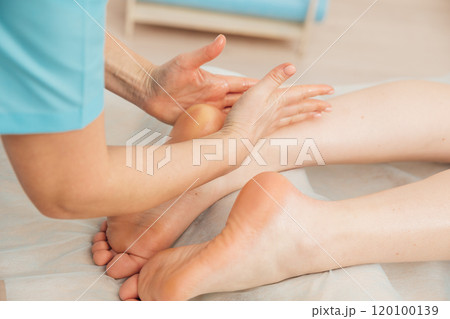 Chiropractor masseur giving foot massage to woman in spa 120100139