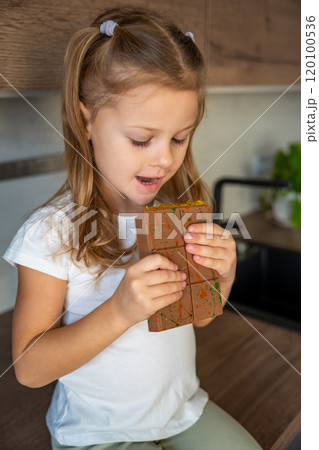 Little girl eating Dubai chocolate with pistachio paste and kataifi dough. Confectionery handmade sweets at home in the kitchen.  120100536