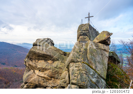 The rocky Oresnik formation features a lookout point and wooden summit cross, offering panoramic views of the Jizera Mountains in Czechia on a cloudy day. 120101472
