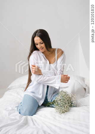 Young happy woman is sitting on a bed with bouquet of flowers Young happy woman is sitting on a bed with bouquet of flowers 120101810