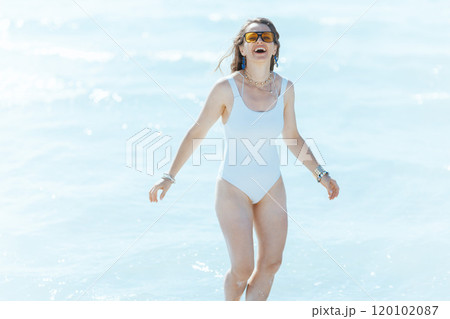 smiling modern woman on ocean shore having fun time in water 120102087