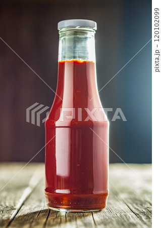 Glass bottle of ketchup on wooden table. 120102099
