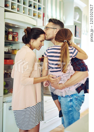 Bound together by love. Shot of a husband lovingly kissing his wife in the kitchen with his family. Bound together by love. Shot of a husband lovingly kissing his wife in the kitchen with his family. 120102927