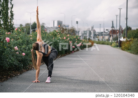 Female athlete practicing a yoga pose on a flower-lined path in an urban park during daytime Female athlete practicing a yoga pose on a flower-lined path in an urban park during daytime 120104340