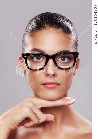 Focus on my face. Studio portrait of a beautiful young woman wearing glasses against a gray background. 120104505